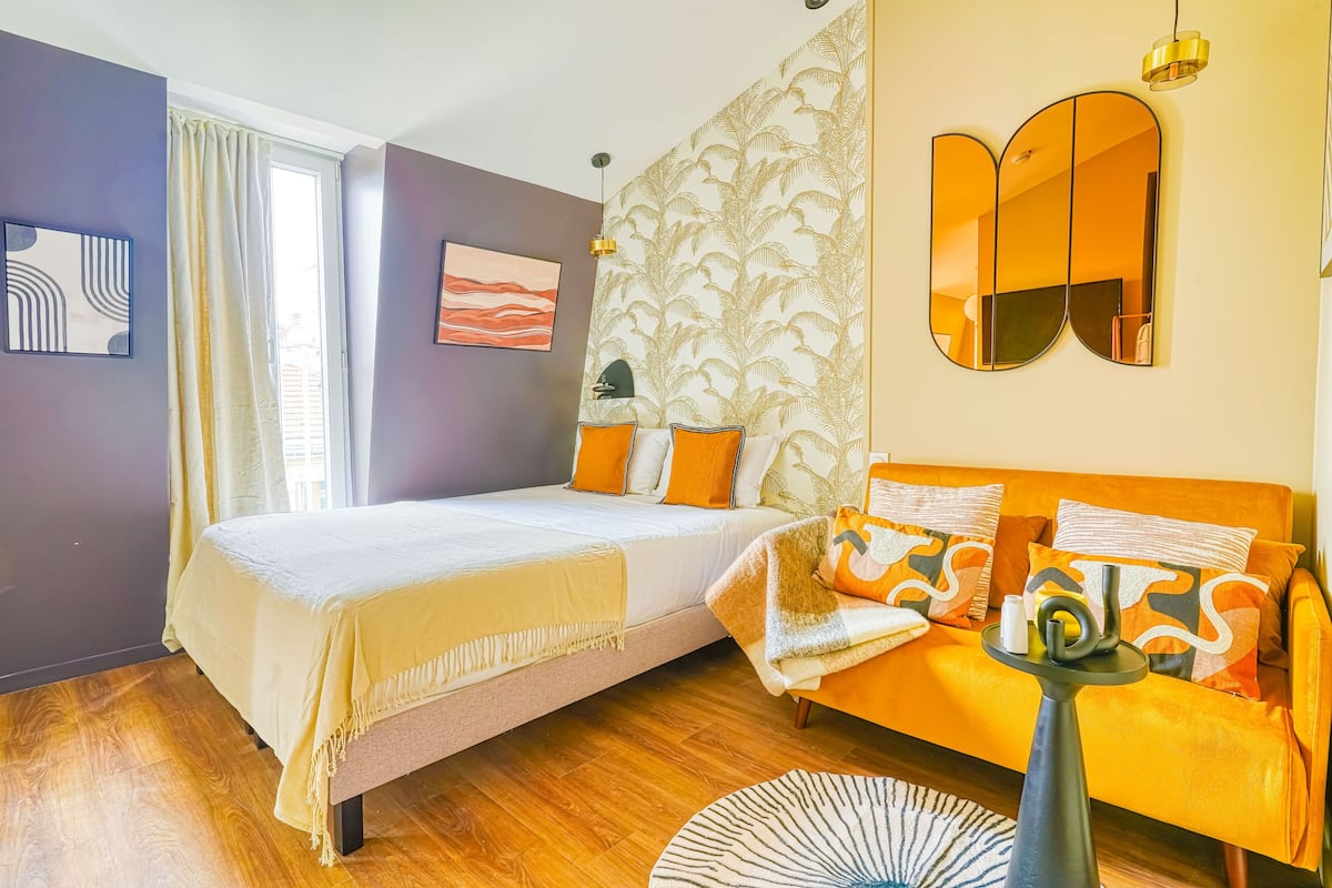 A modern bedroom with a bed, sofa, and a mirror.