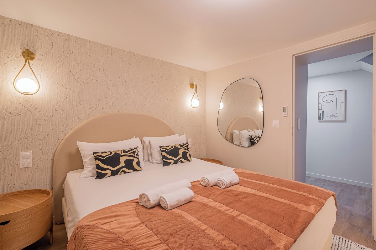 A hotel room with a large bed, two bedside lamps, a round mirror, and a painting on the wall.