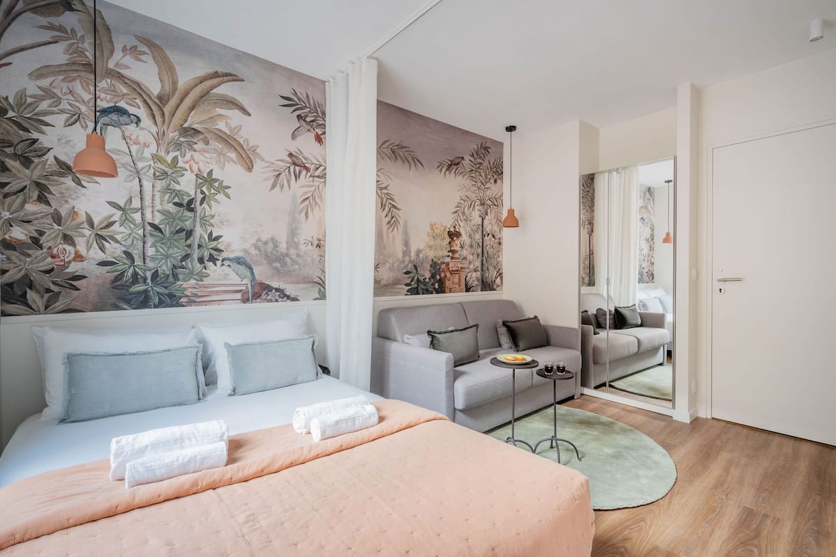 A bedroom with a bed, a sofa, a small table, and a mirror.