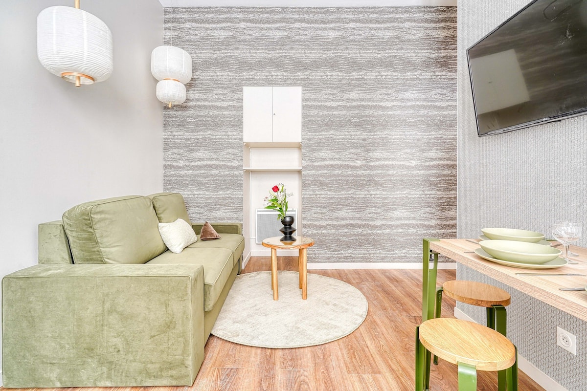 A modern living room with a green sofa, a round rug, a small wooden table, and a TV mounted on the wall.