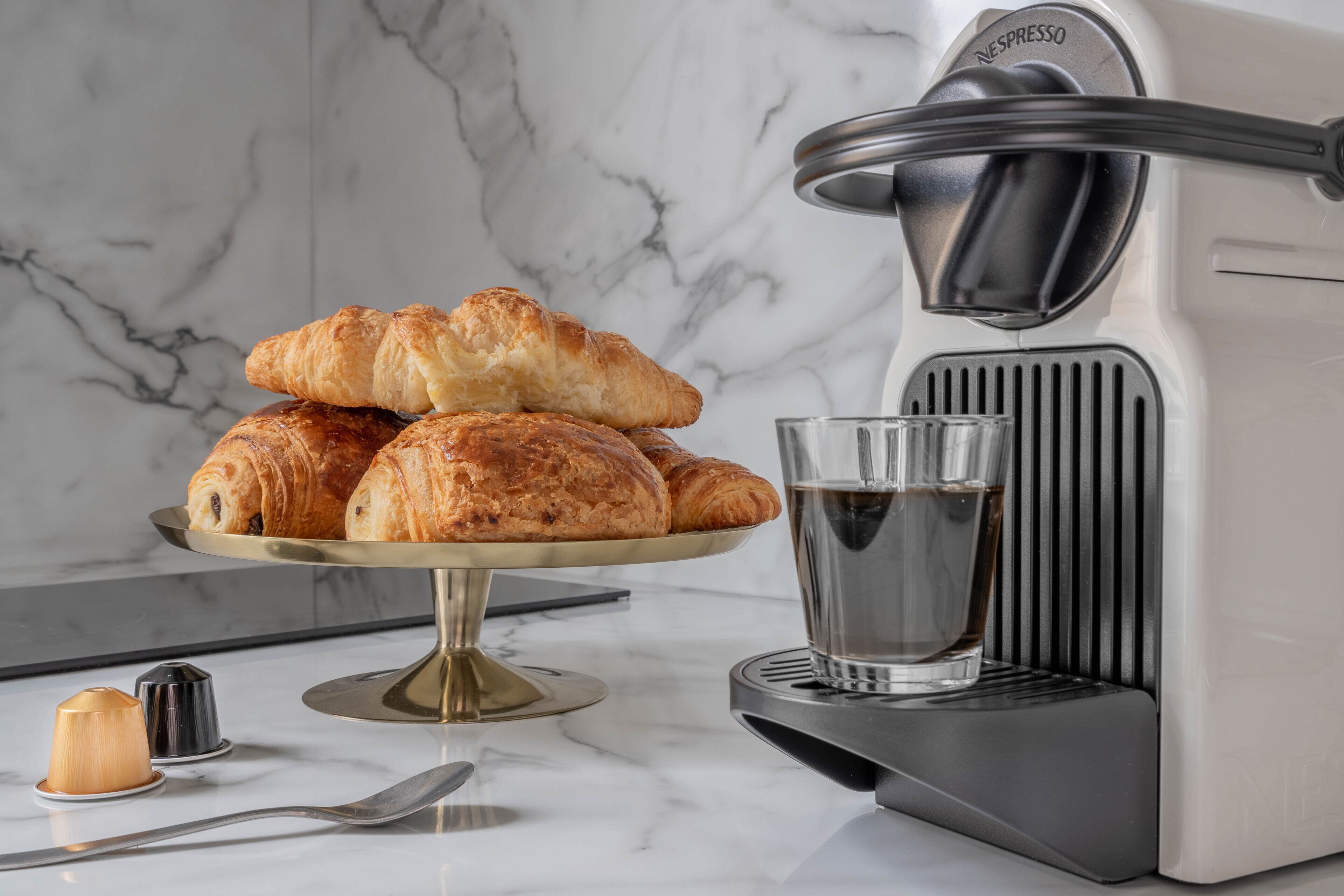 A kitchen with a coffee machine, a glass of water, and a plate of croissants.