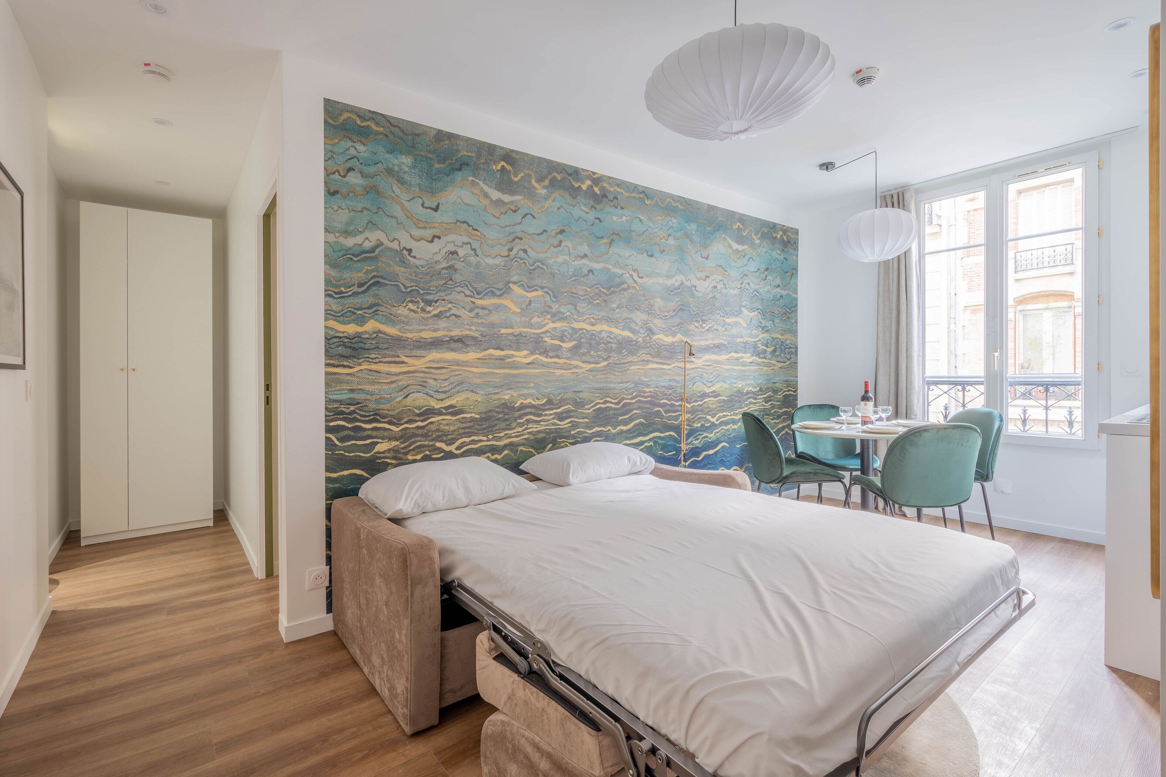 A modern bedroom with a bed, a mural on the wall, a dining area with chairs, and a window with a view.