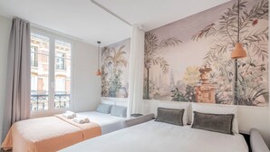A hotel room with two beds, a large window with curtains, a mural of tropical plants, and a hanging pendant light. - Residence Le Belleville (Paris)
