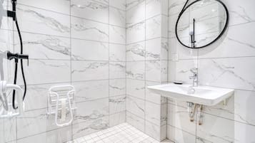 Een badkamer met witte marmeren tegels, een ronde spiegel, een wastafel en een douchehoek.