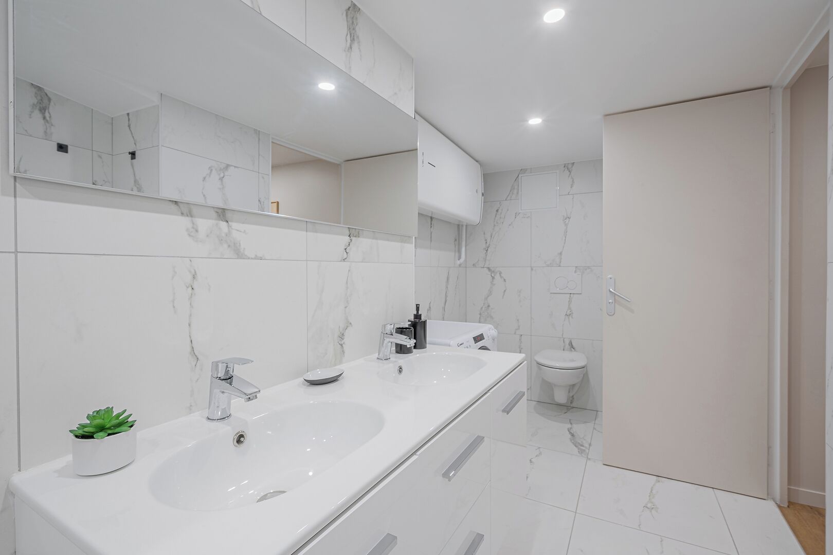 A modern bathroom with two sinks, a large mirror, and a toilet.