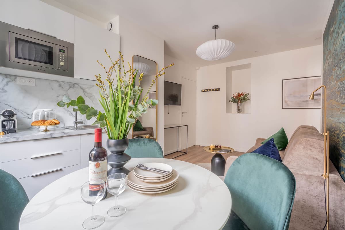 A modern kitchen with a microwave, a dining table set with plates, wine glasses, and a bottle of wine. There is a vase with flowers on the table.