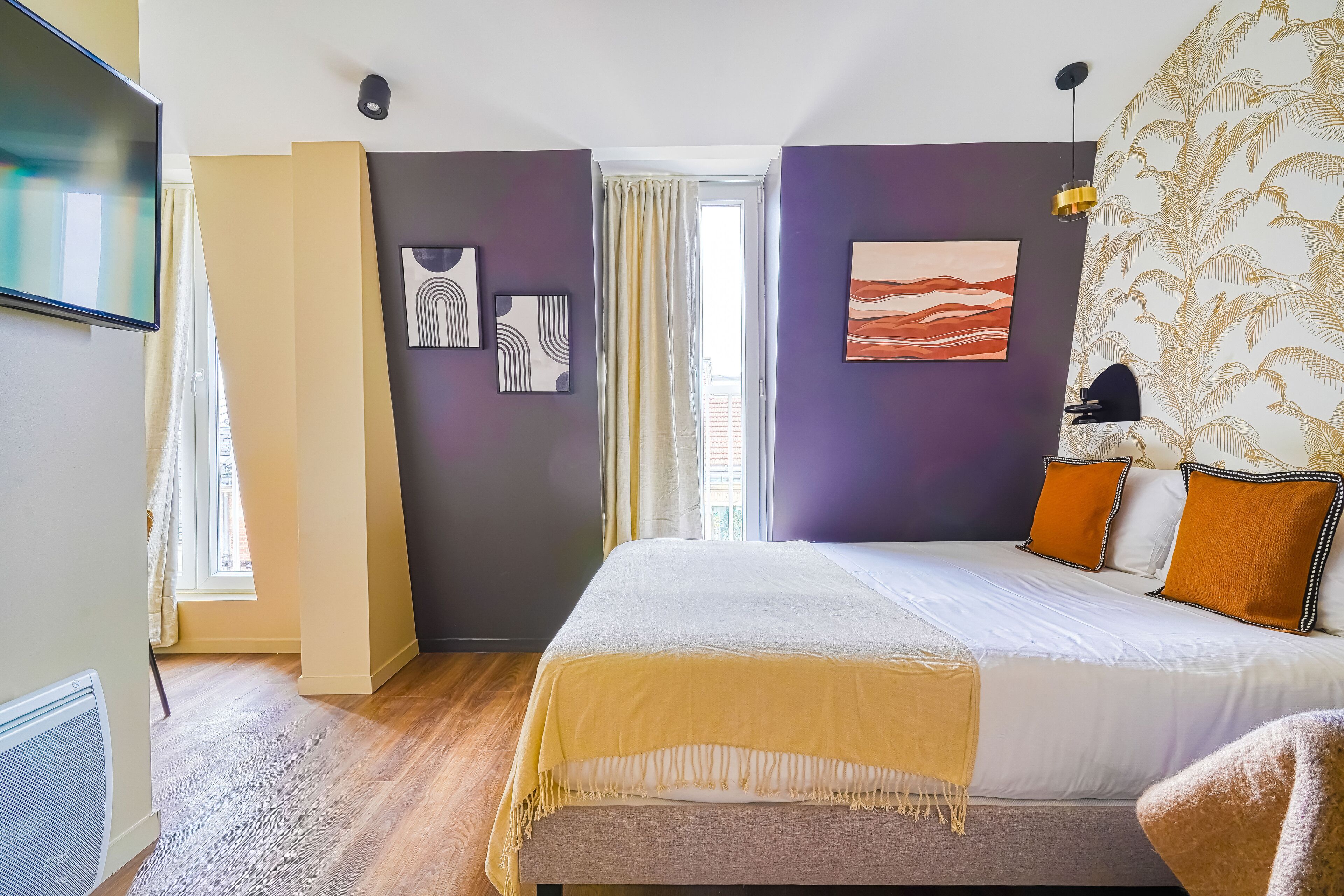 Une chambre moderne avec un grand lit, un téléviseur à écran plat et des œuvres d’art accrochées aux murs.