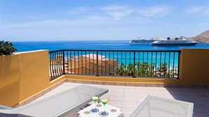 A balcony with two lounge chairs and a small table, overlooking a clear blue sea and a cruise ship. - The Best of Cabo San Lucas! (cabo san lucas)