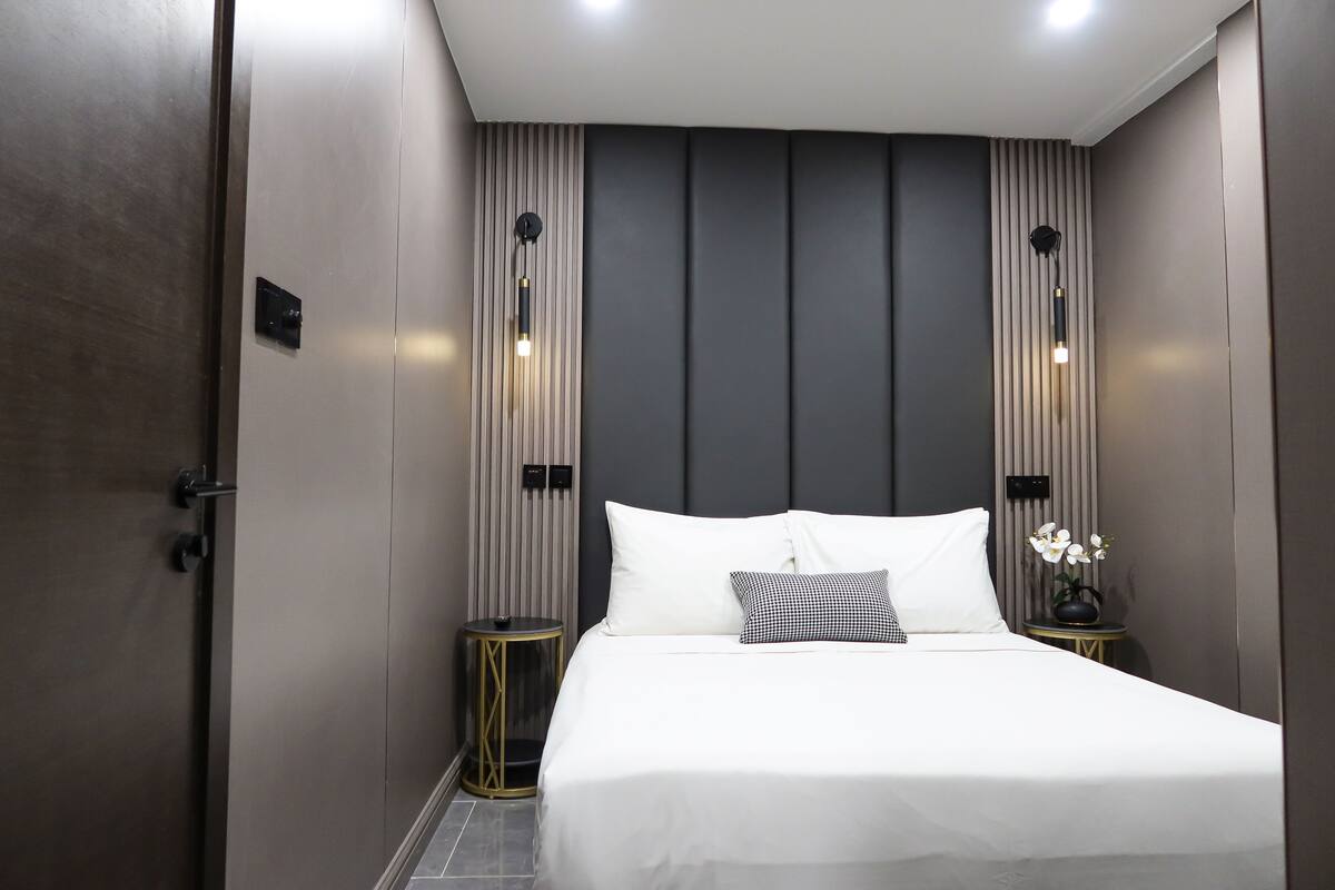 A modern hotel room with a large bed, two bedside tables, and a nightstand with a vase of flowers.