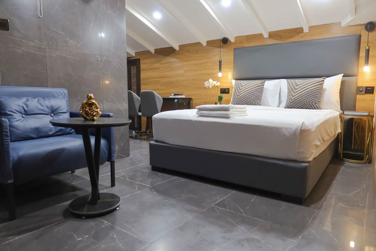 A modern hotel room with a large bed, a blue sofa, a small round table, and a decorative golden statue.