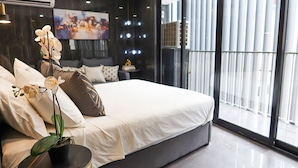 A modern bedroom with a large bed, a potted orchid, and a view of the city through large windows. - Recharge Residences  (Singapore)
