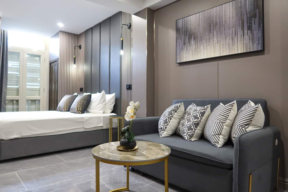 A modern bedroom with a bed, a sofa, a small round table, and a wall-mounted artwork.