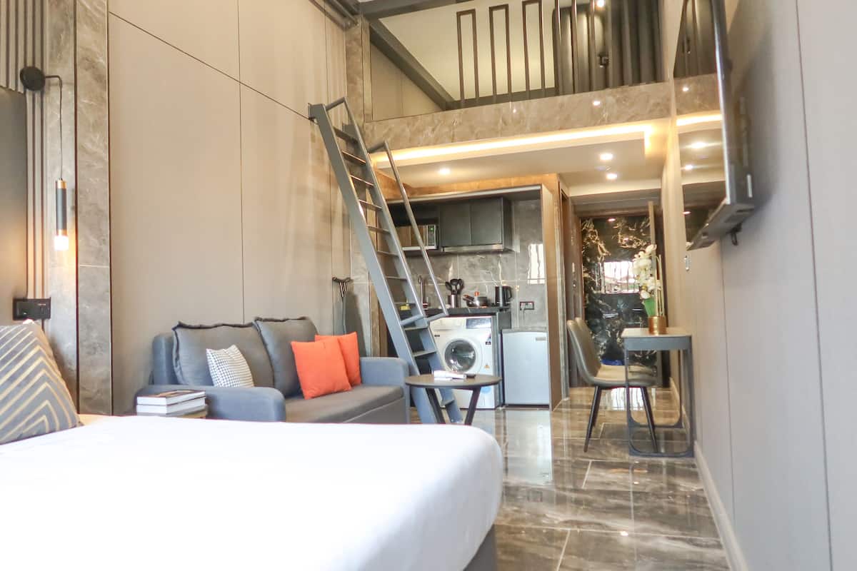 A modern hotel room with a bed, a sofa, a dining area, and a kitchen.