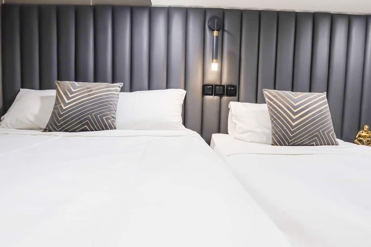 A modern hotel room with a large bed, two pillows with geometric patterns, a wall-mounted light fixture, and a small golden statue on the nightstand.