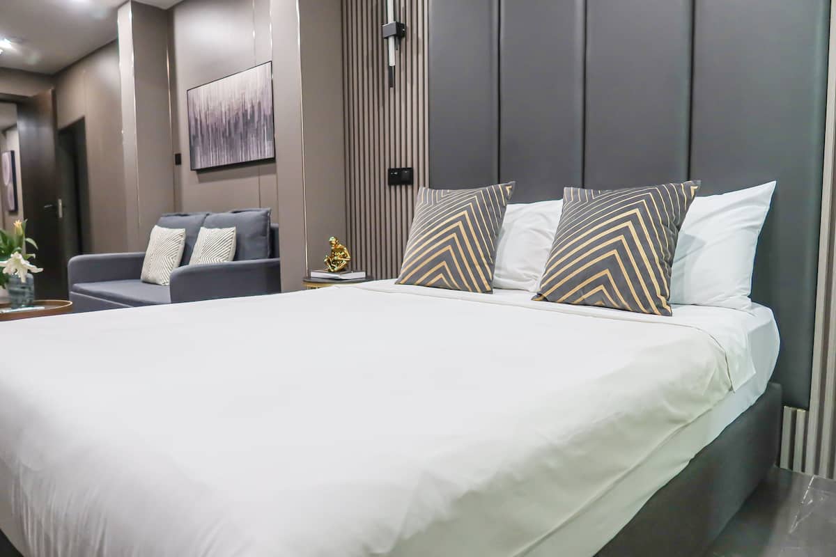 A modern hotel room with a large bed, grey upholstered sofa, and a decorative wall piece.