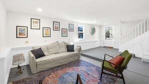 Un salon spacieux avec un canapé beige, un tapis à motifs et des tableaux encadrés accrochés au mur.