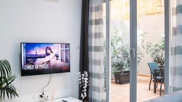 Una sala de estar moderna con un televisor de pantalla plana, un sofá, un mueble blanco para entretenimiento y un ventanal corredizo que da a un patio exterior.