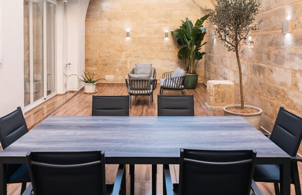 Un salón de conferencias con una larga mesa, seis sillas, dos plantas en macetas y una pared de piedra.