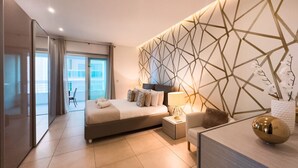 A modern hotel room with a large bed, a desk, and a decorative wall. - Luxury Seafront 3BR w/Pool by ArcoCollection (Sliema)