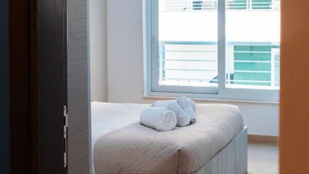 A bedroom with a bed, a hanging light fixture, and a window with blinds. - Luxury Seafront 3BR w/Pool by ArcoCollection (Sliema)