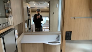 A compact bathroom with a toilet, sink, and built-in storage cabinets. - 2020 Leisure Travel Rv Wonder at Boothbay Harbor, Maine!   (Boothbay)
