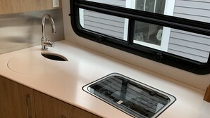 A compact kitchen with a white countertop, a stainless steel sink, and wooden cabinets. - 2020 Leisure Travel Rv Wonder at Boothbay Harbor, Maine!   (Boothbay)