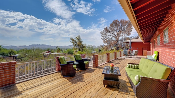 Une terrasse en bois, aménagée avec du mobilier d’extérieur, notamment un canapé et des fauteuils, qui offre une vue imprenable sur un paysage magnifique, avec des montagnes et des arbres.