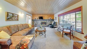 Un salon spacieux doté d’une cheminée en pierre, d’un plafond en bois et de grandes fenêtres.
