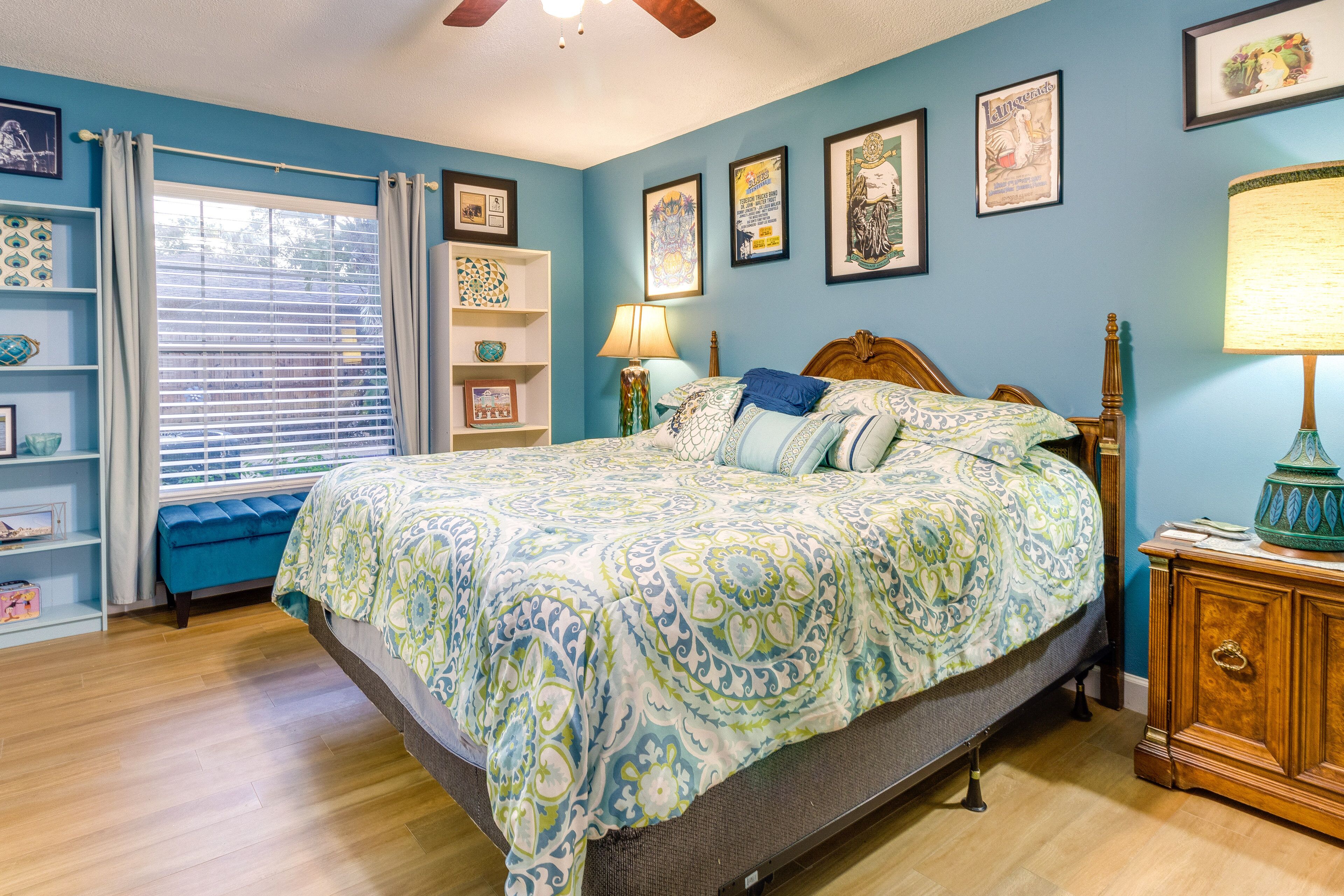 Une chambre avec un grand lit, une tête de lit en bois, une table de chevet avec une lampe, une commode et une fenêtre avec des rideaux.