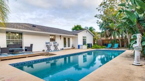 A residential backyard with a swimming pool, patio furniture, and a white house.