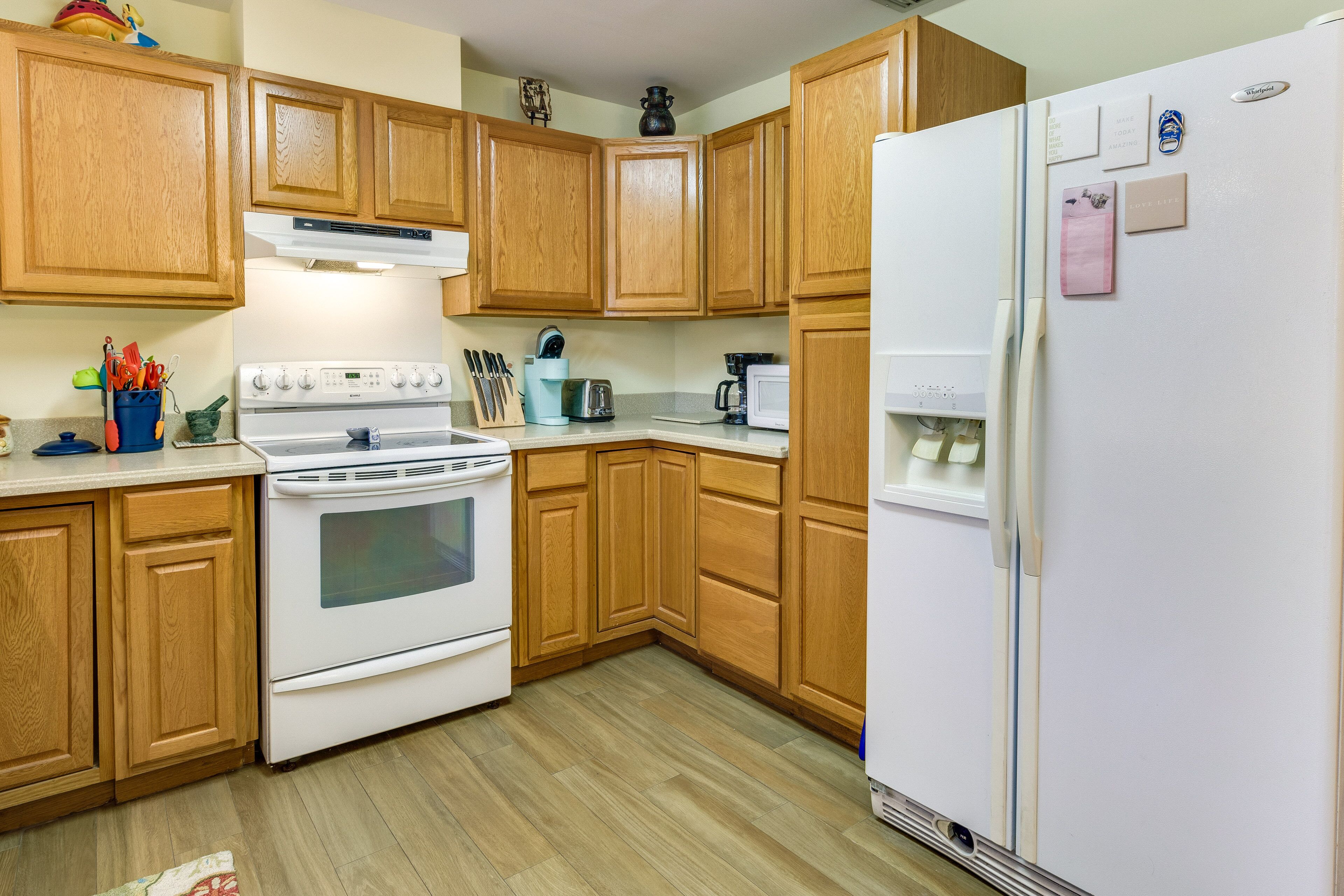 A kitchen with wooden cabinets, a white stove, a refrigerator, and various kitchen appliances.
