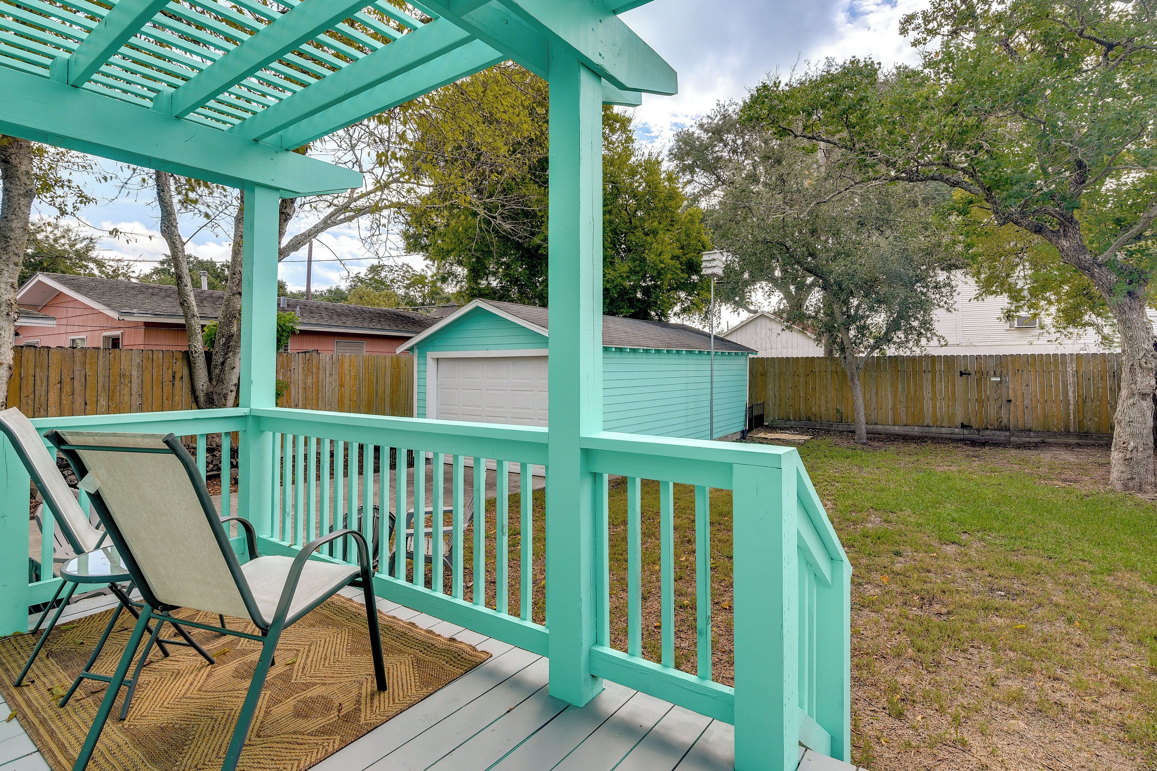 A turquoise deck with a pergola, a chair, and a shed in a backyard.