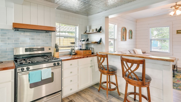 A kitchen with a stainless steel stove, white cabinets, and a wooden bar stool.