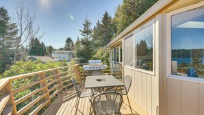Eine Holzterrasse mit Tisch, Stühlen, einem Grill und Blick auf Bäume sowie ein Haus im Hintergrund.