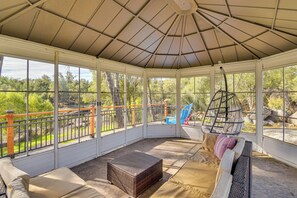 A covered patio with a view of a wooded area, a hanging chair, and a cushioned seating area. - Private Lake, Hot Tub & EV Charger: Mariposa Home! (Mariposa)