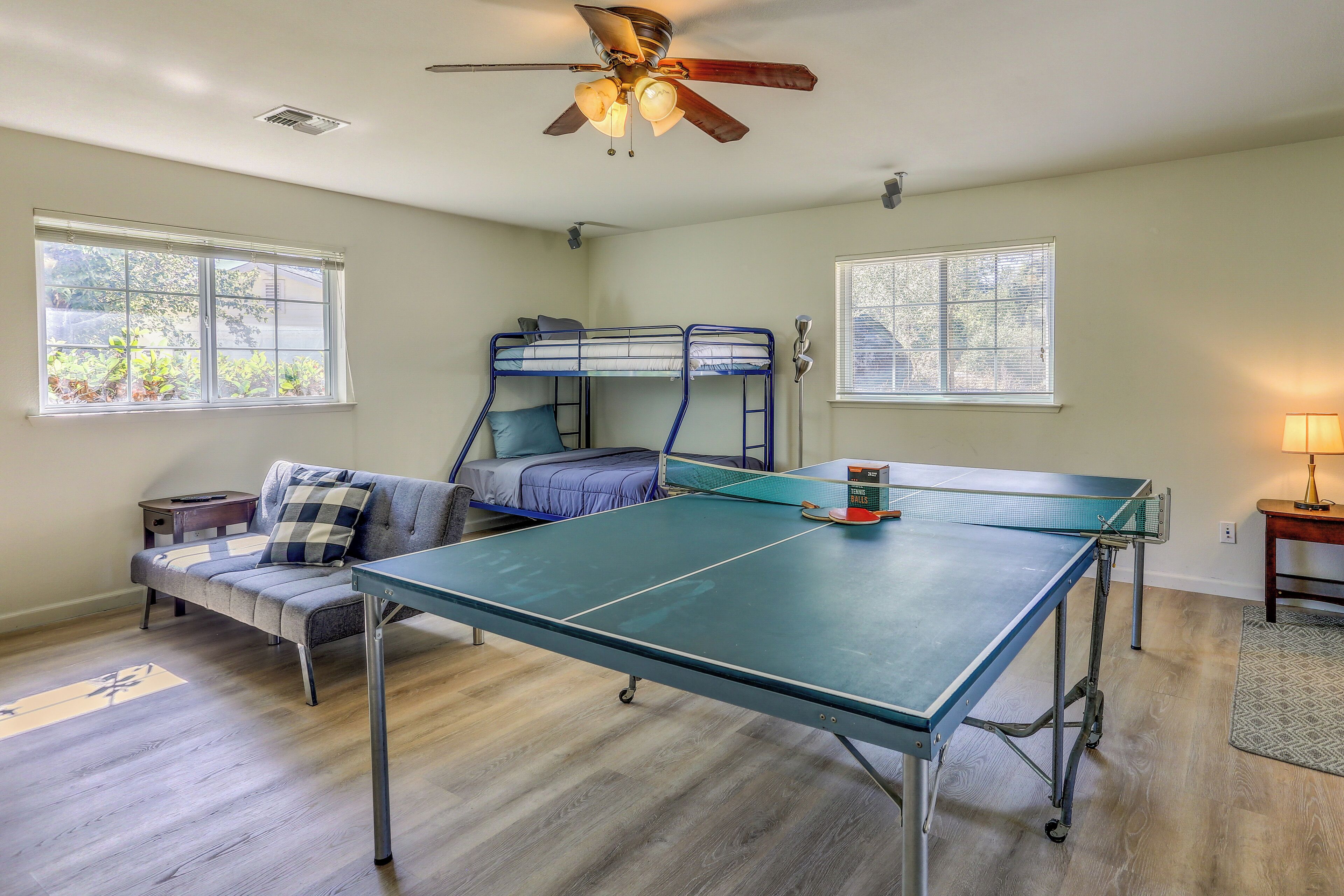 A room with bunk beds, a ping pong table, a ceiling fan, and two windows.