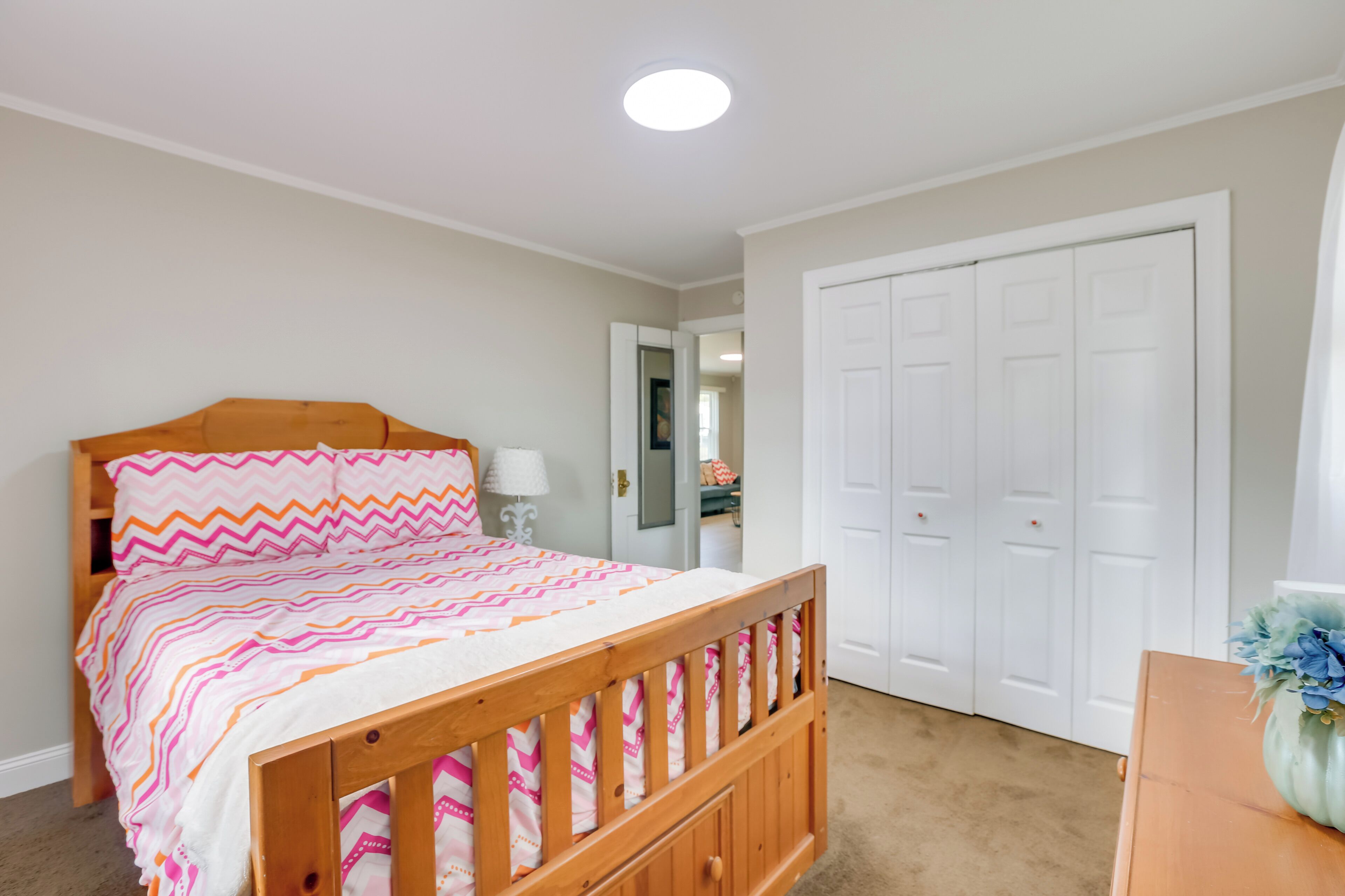 A bedroom with a wooden bed, a white door, and a small table with a vase.