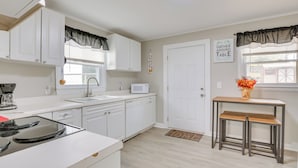 Una cocina moderna con armarios blancos, microondas, pileta y una mesa de madera con bancos.