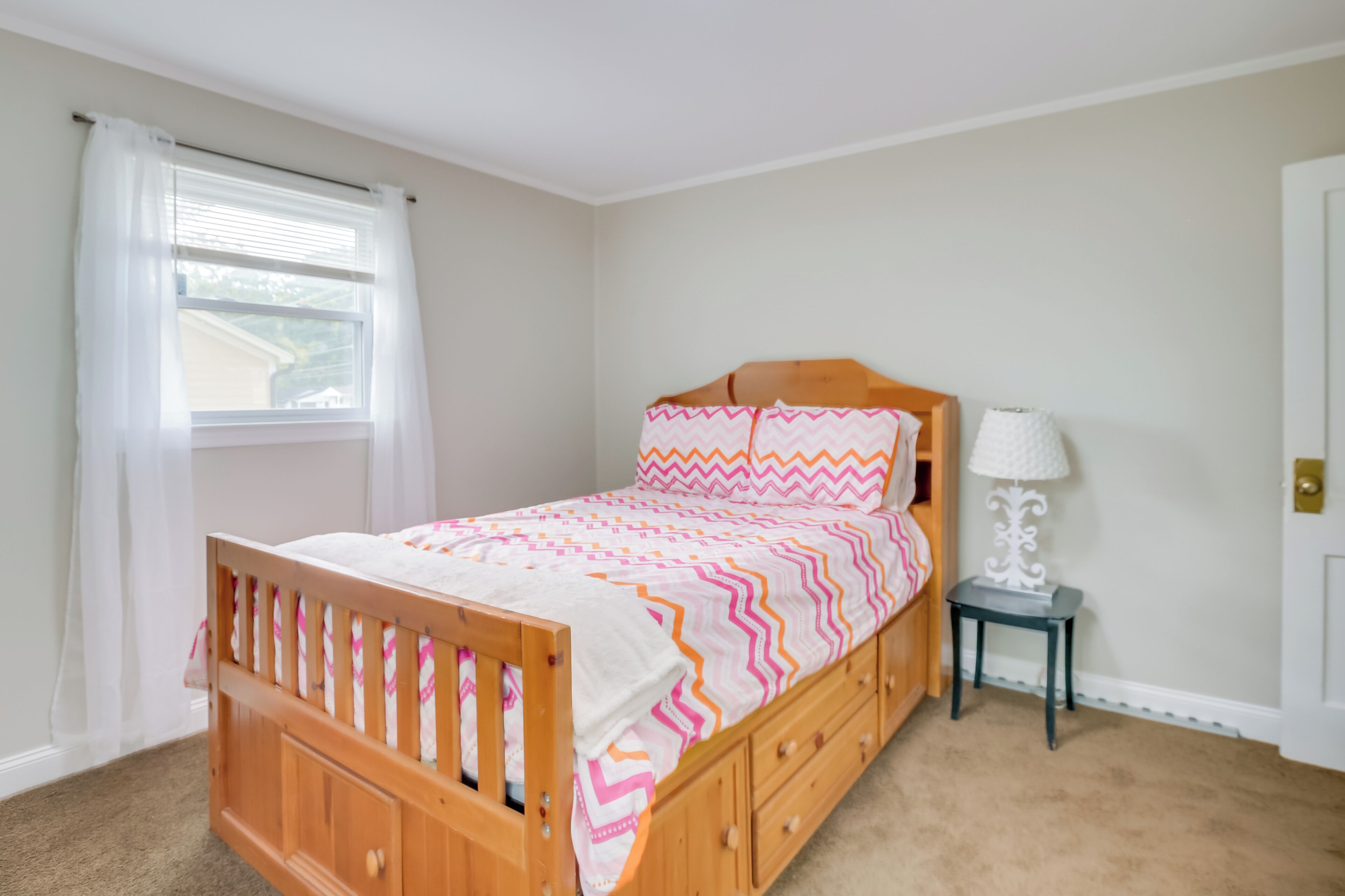 A bedroom with a wooden bed, a nightstand, a lamp, and a window with curtains.