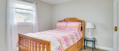 A bedroom with a wooden bed, a nightstand, a lamp, and a window with curtains.