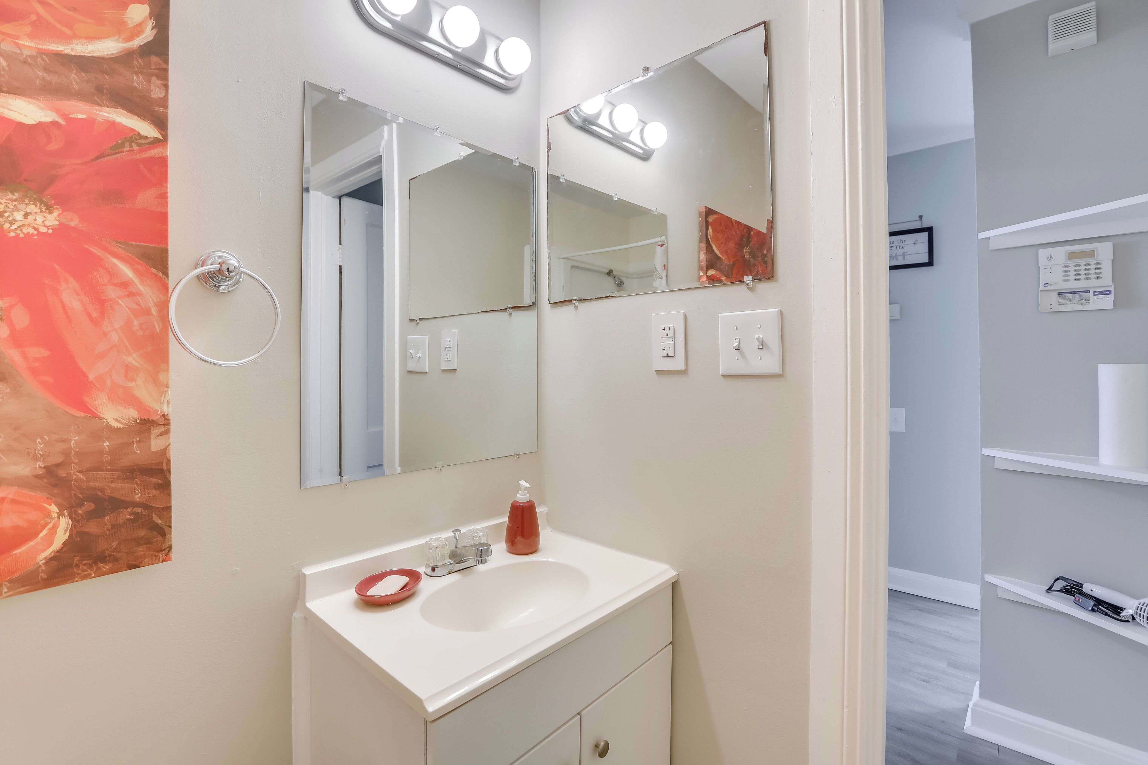 A bathroom with a white sink, two mirrors, and a ring light.