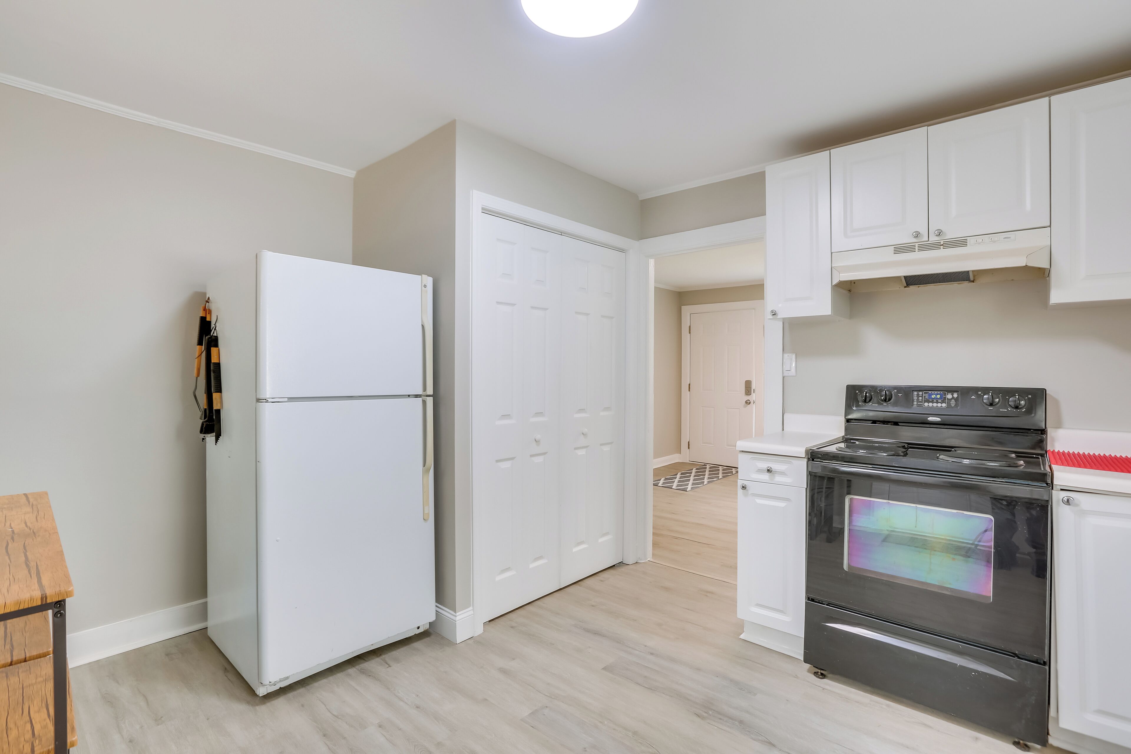 A kitchen with white cabinets, a white refrigerator, a black oven, and a wooden table.