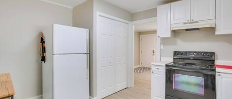 A kitchen with white cabinets, a white refrigerator, a black oven, and a wooden table.