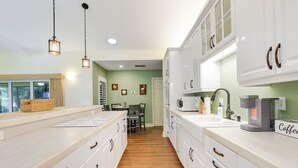 A modern kitchen with white cabinets, wooden countertops, a coffee maker, and a dining area with a table and chairs. - Pet-friendly Fort Pierce Home w/ Screened Porch! (Fort Pierce)