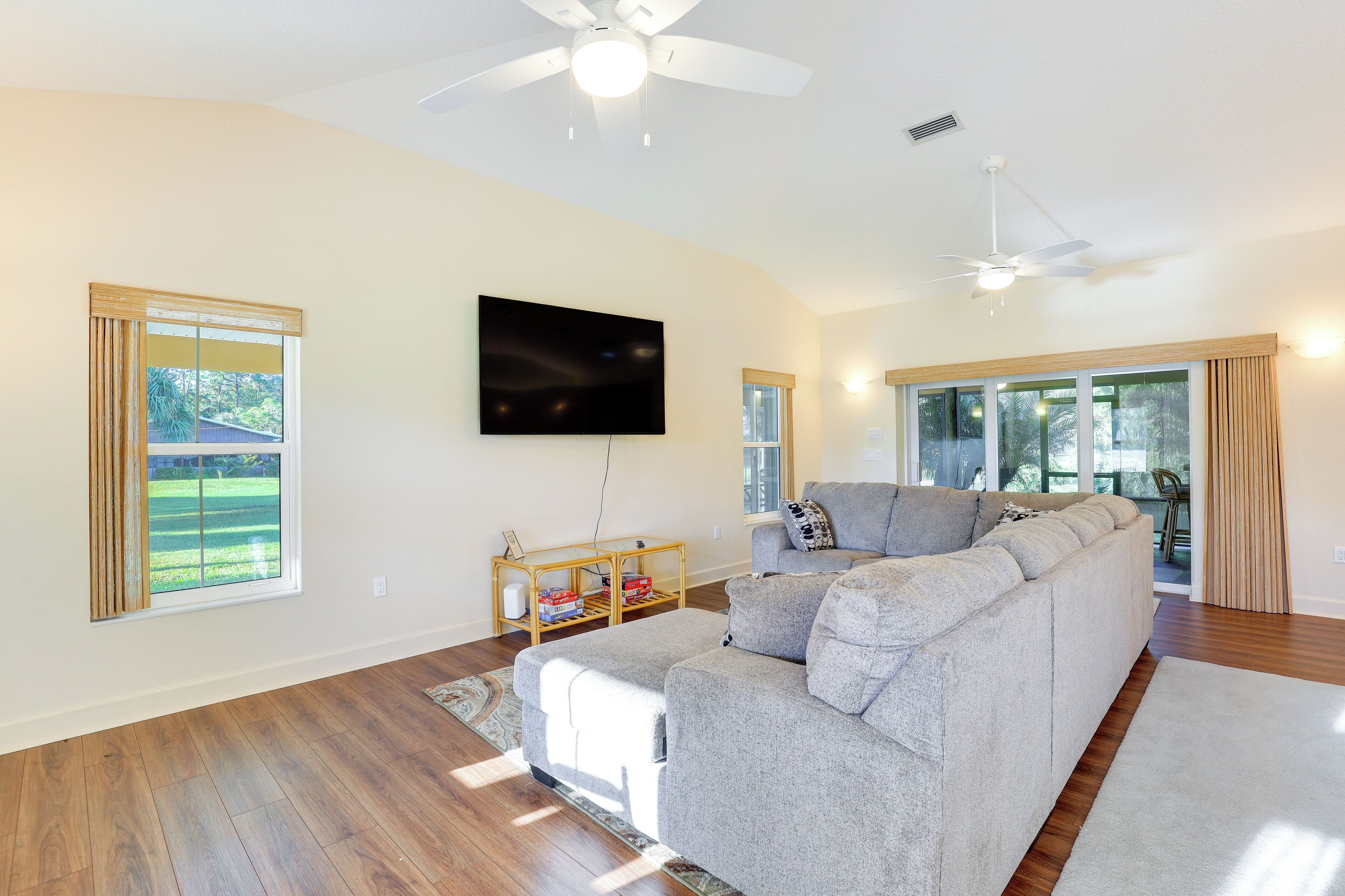 A spacious living room with a large gray sectional sofa, a flat-screen TV mounted on the wall, and a ceiling fan.