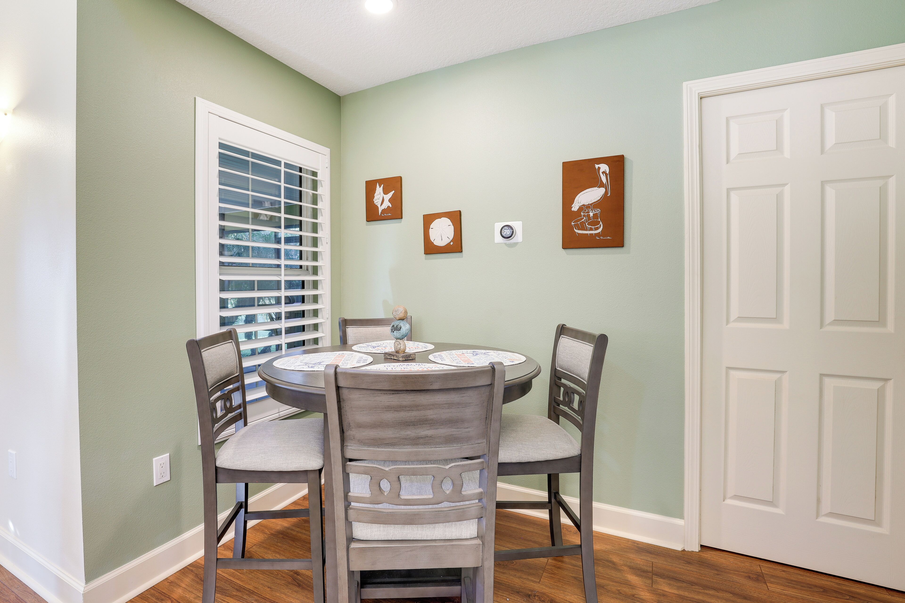 A dining area with a round table, four chairs, and a window with blinds.