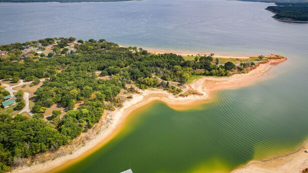 An aerial view of a coastal area with a beach, dense greenery, and a clear view of the water. - Lake Texoma Vacation Rental: 1 Mi to Boat Ramp! (Pottsboro)