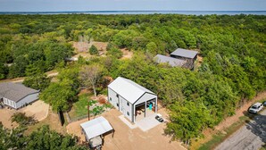 An aerial view of a property with a large open garage, a house with a sloped roof, and a dirt driveway. - Lake Texoma Vacation Rental: 1 Mi to Boat Ramp! (Pottsboro)