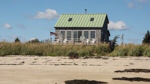 Een strandhuis met een groen dak, een veranda en een Amerikaanse vlag.