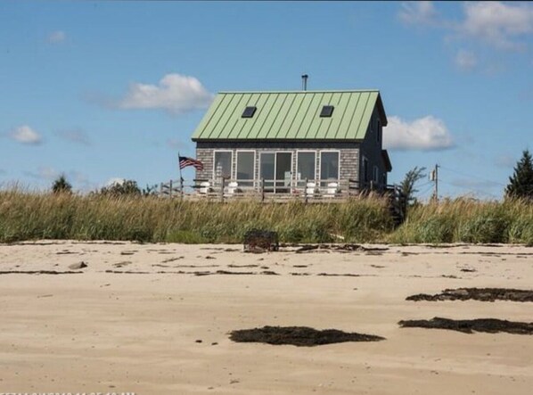 A beach house with a green roof, a porch, and an American flag.